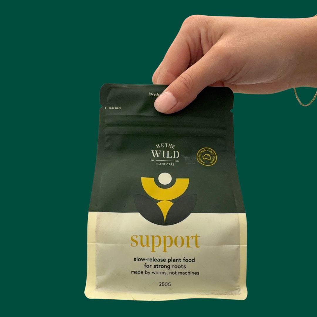Hand holding a We the Wild Support Slow Release Plant Food 250g package
